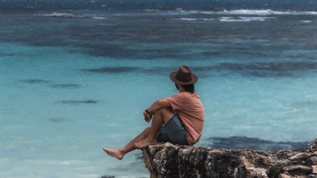 man sitting on cliff edge looking out to sea